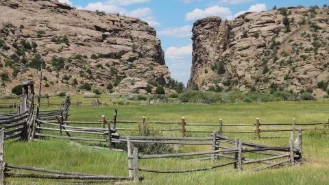 wood corral in a meadow in front of a large cleft between two rocky cliffs